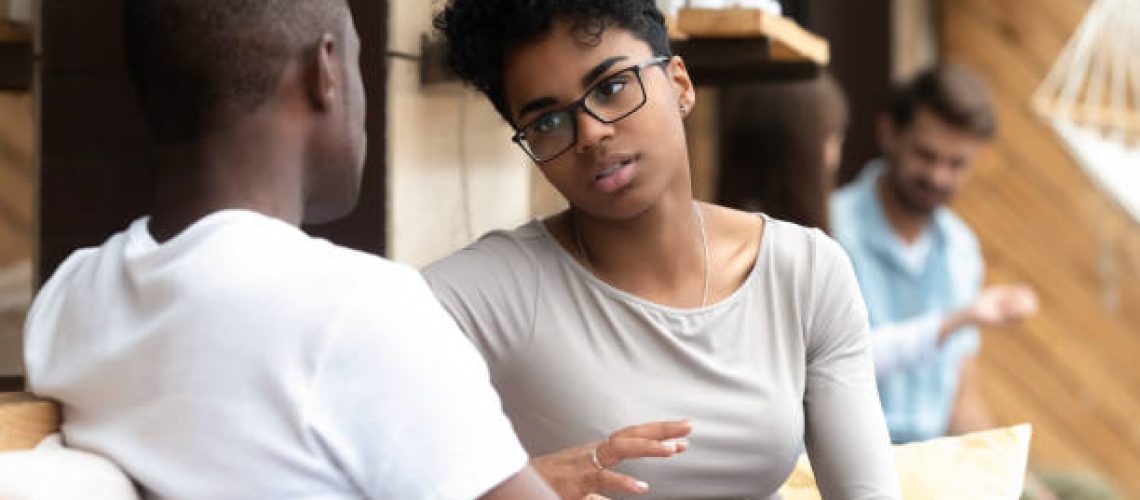 Focused African American woman talking with man in cafe, girlfriend discussing relationships with boyfriend, explaining, gesticulating, friends having serious conversation, sitting together on couch